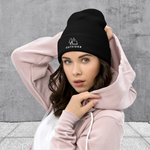 Woman in Black knit beanie with embroidered "Outsider" graphic of tent, tree, and moon